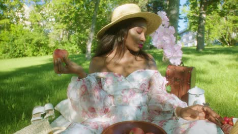 mujer negra comiendo manzana y mirando alrededor en un picnic en el parque