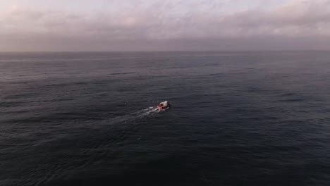 aerial view flying towards fishing boat on quiet ocean waves cloudy sunset seascape