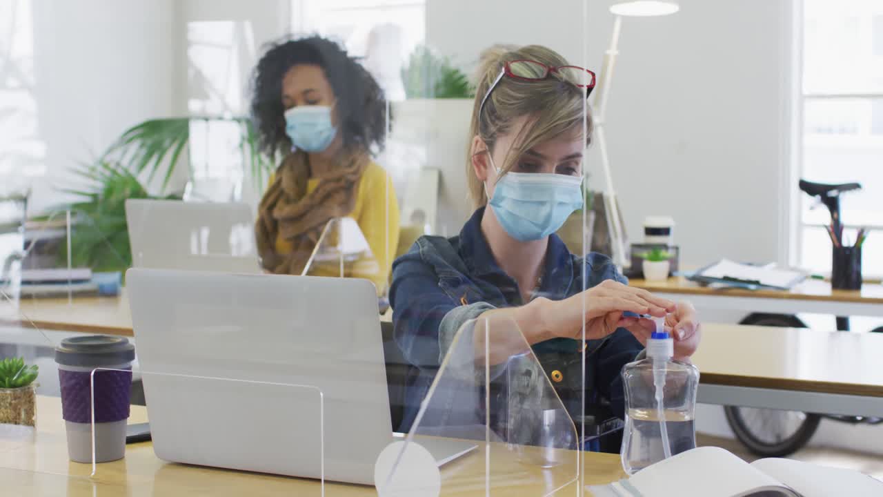 Woman wearing face mask sanitizing her hands at office