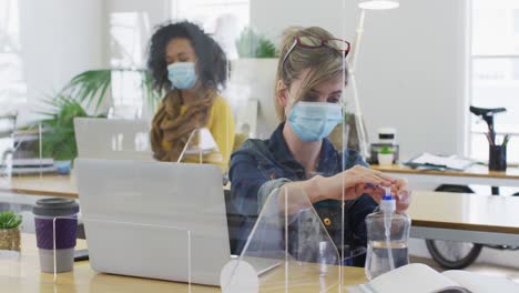 woman wearing face mask sanitizing her hands at office