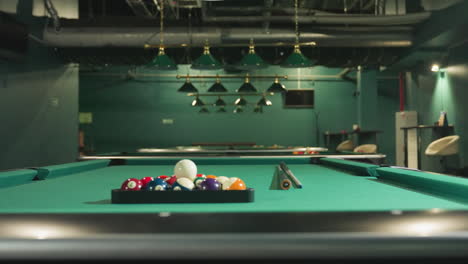 shot of green pool tables with billiard balls arranged on them and cue sticks placed across the table. overhead lamps provide soft lighting in billiard room, creating an inviting atmosphere