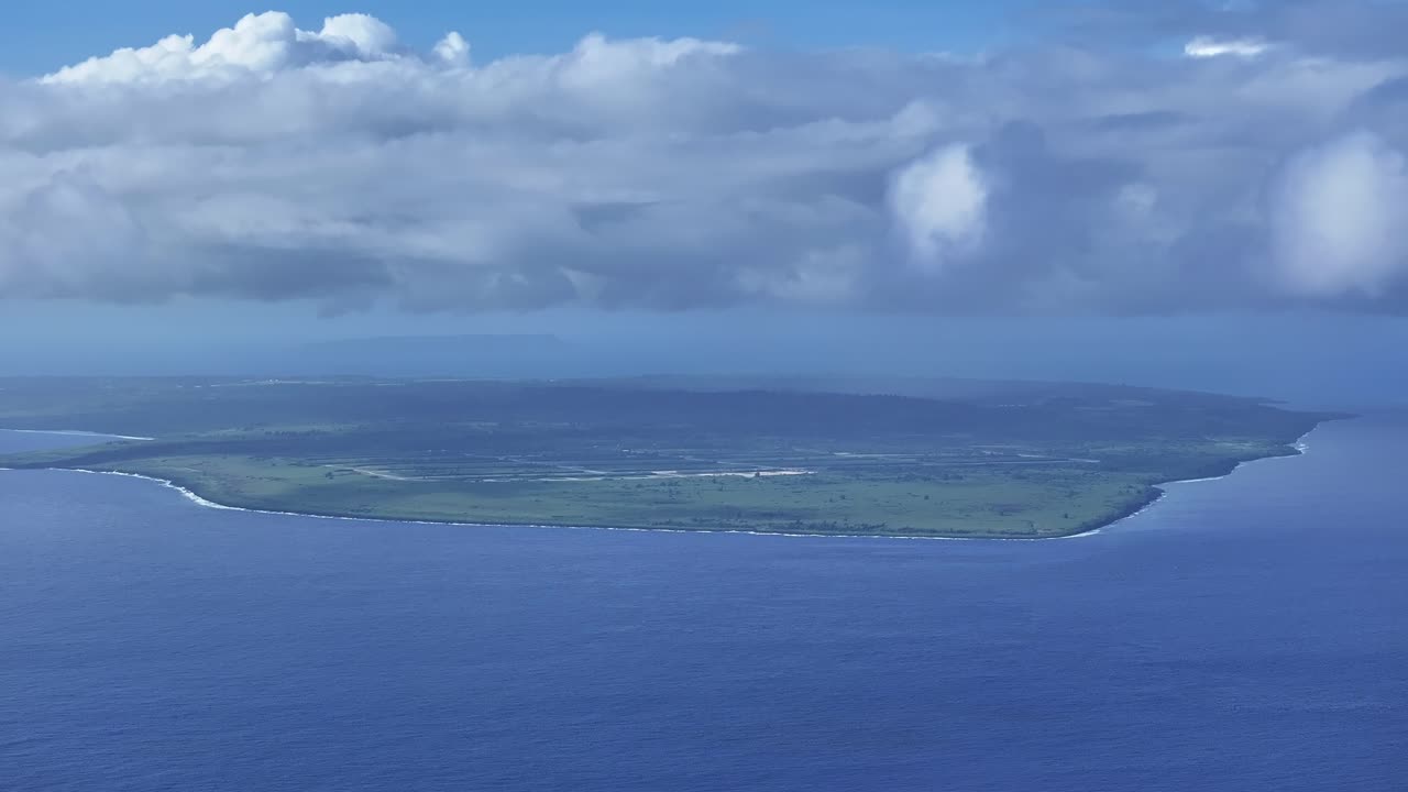 "A sweeping aerial view looking south from the beautiful west coast of Saipan toward Tinian Island. The deep blue Saipan Channel and turquoise lagoon provide a stunning backdrop for travel and nature