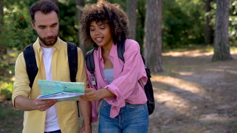 young black hiker female with backpack and caucasian man with map walk on a forest trail. medium shot, front view.