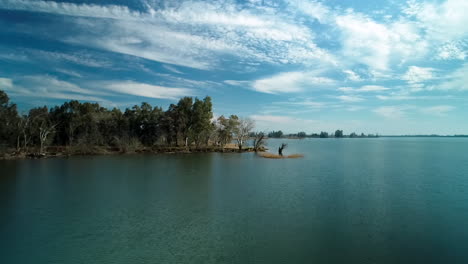 aerial shot moving inland across a lake, toward a peninsula overcrowded by trees