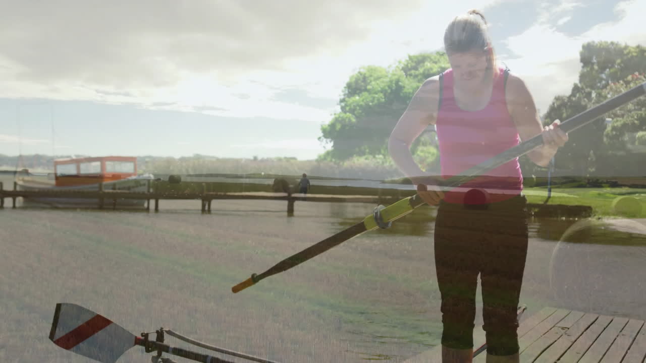 Preparing rowing equipment by lakeside, woman with trees in background