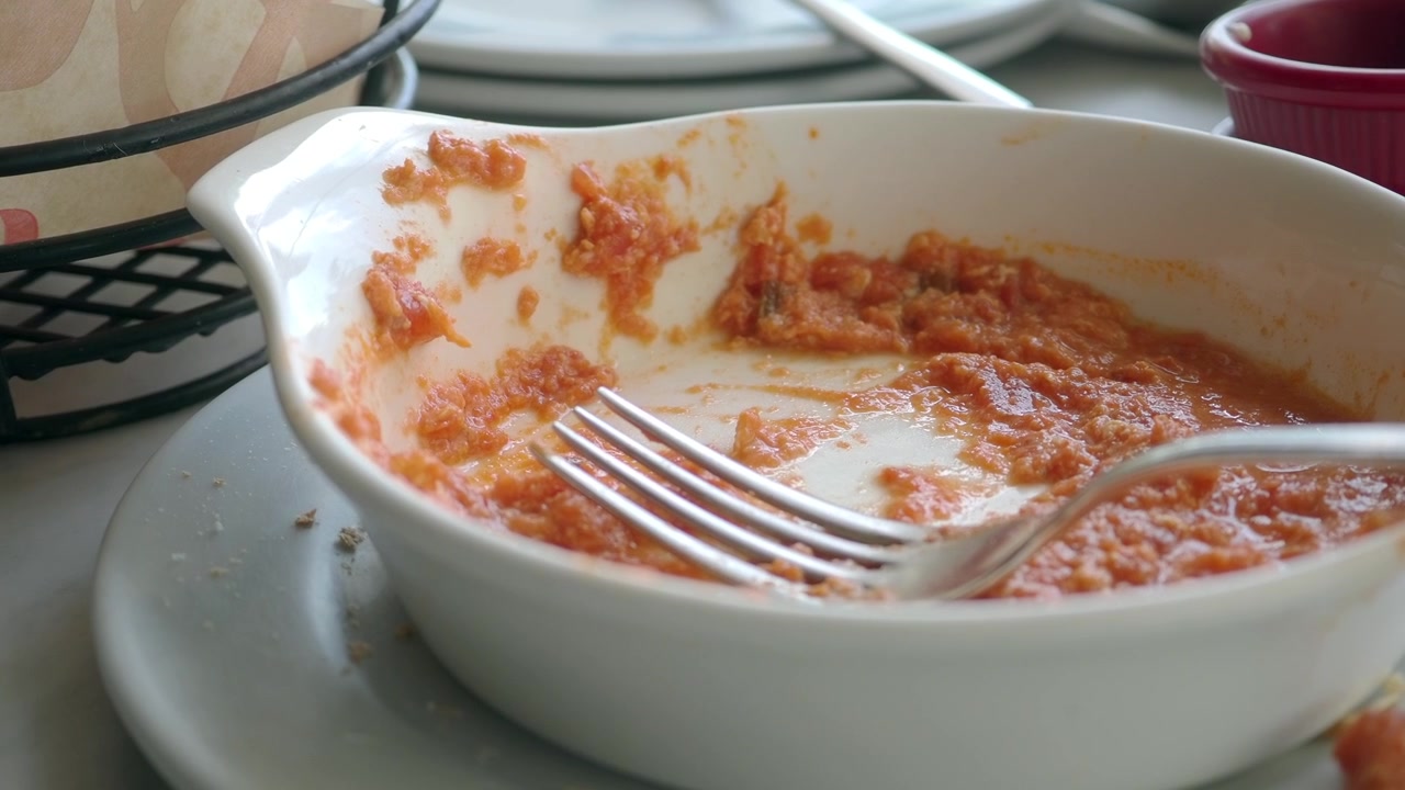 Primo piano di una ciotola bianca con avanzi di salsa rossa e una forchetta