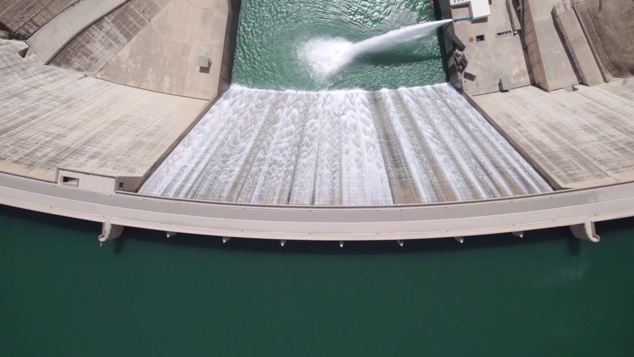 Presa operativa liberando agua, con la central hidroeléctrica descargando agua tras la generación de turbina. Vista aérea cenital ascendente. Central hidroeléctrica. Presa de Rules. España.