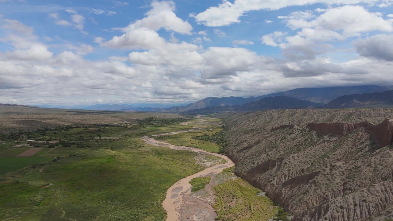 Ripresa aerea all'indietro del Rio Calchaqui che attraversa una valle lussureggiante accanto a colline aspre, terreni agricoli fertili della pianura alluvionale