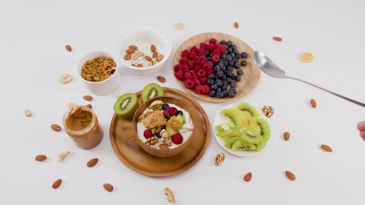 Vista dall'alto di una mano che prende un cucchiaio da una ciotola di yogurt con granola e frutta.