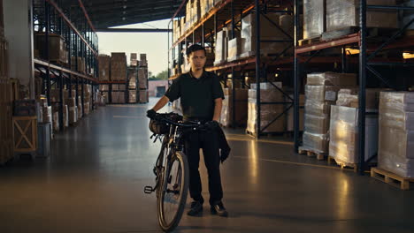 A delivery worker stands with a bicycle in a large warehouse