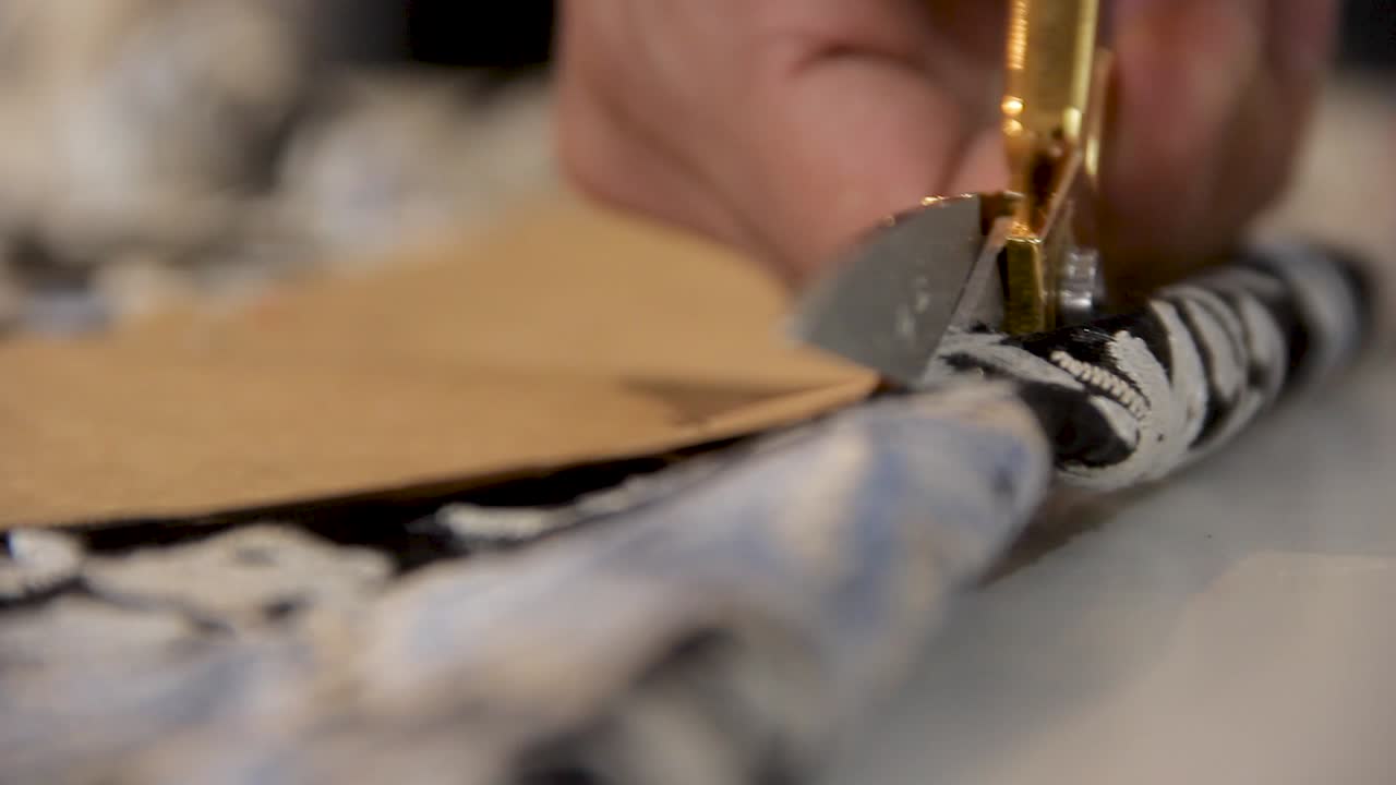 macro cierre de manos masculinas de modista cortando tela texturizada de flores con tijeras de un patrón de costura - profundidad de campo poco profunda con enfoque selectivo disparo interior de mano luz natural