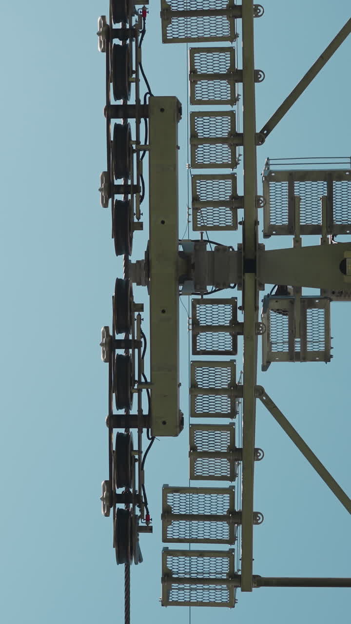 Contemporary cable way support pole with crossarms and moving gondolas under clear blue sky on sunny day view from bottom slow motion