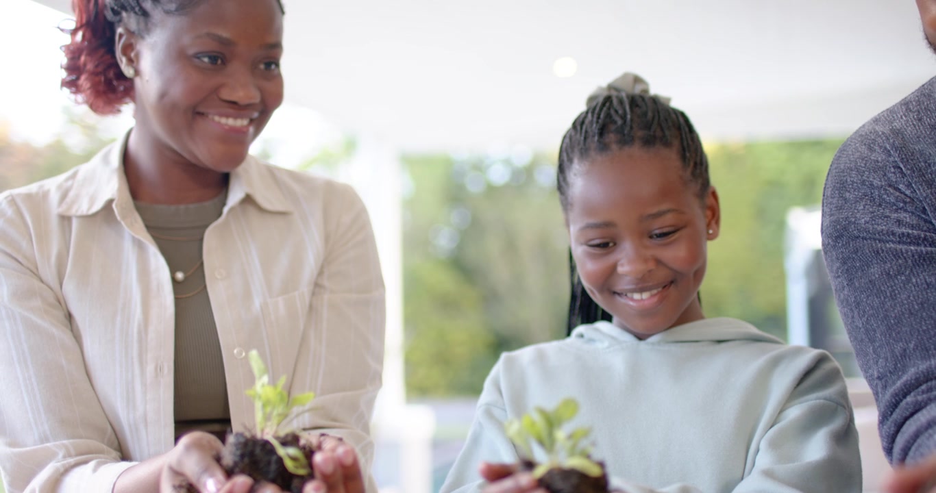 African family holding seedlings with soil on porch while camera pulling back, sharing pride