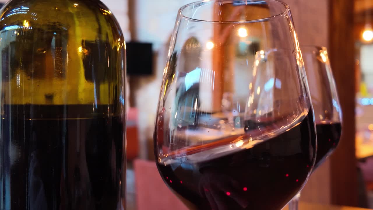 Vino rosso che volteggia in un bicchiere accanto a una bottiglia sotto una calda illuminazione interna.
