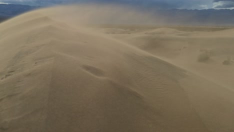 Arena-En-Cámara-Lenta-Que-Sopla-Sobre-La-Cresta-De-Una-Duna-De-Arena,-Panorámica-Desde-El-Valle-Hasta-La-Cima-De-La-Duna