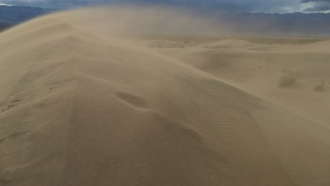 arena en cámara lenta que sopla sobre la cresta de una duna de arena, panorámica desde el valle hasta la cima de la duna