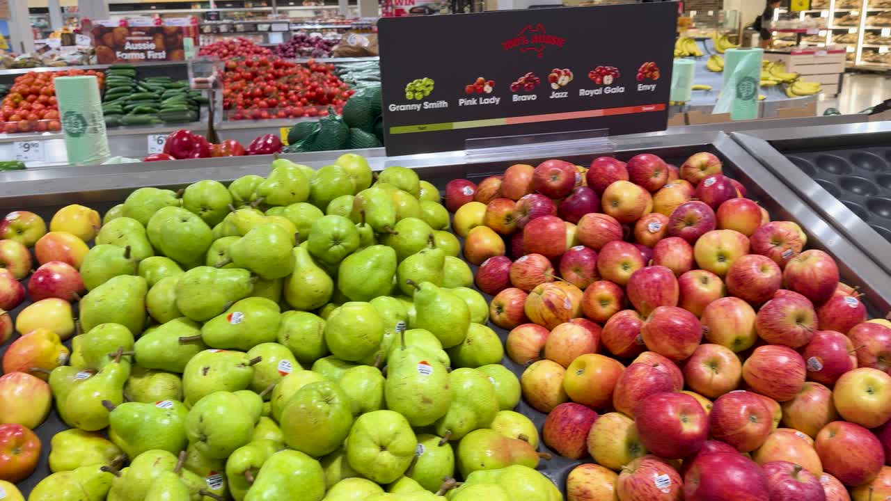 A slow panning shot across organized rows of fresh green pears and red apples