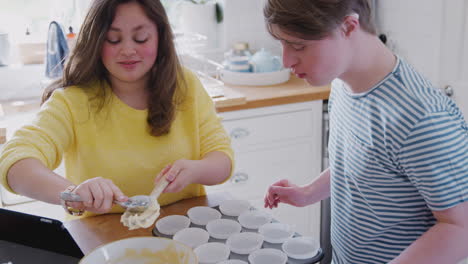young downs syndrome couple putting mixture into paper cake cases in kitchen at home