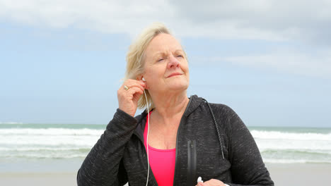 Front-view-of-old-caucasian-senior-woman-listening-music-on-earphones-at-beach-4k