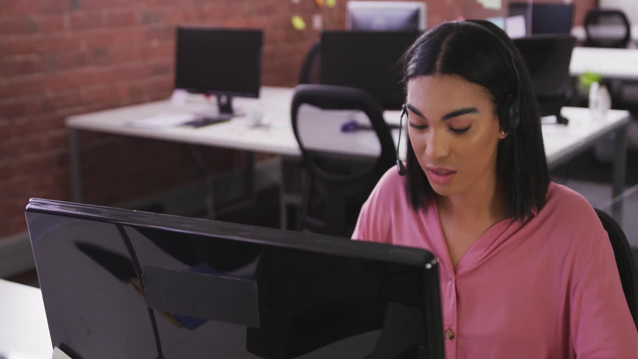 mujer de negocios de raza mixta con auriculares sentada en el escritorio haciendo una videollamada