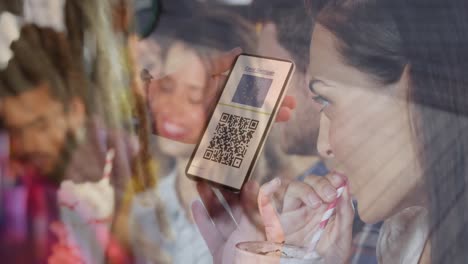 woman holding a smartphone with qr code on screen against caucasian woman drinking a smoothie