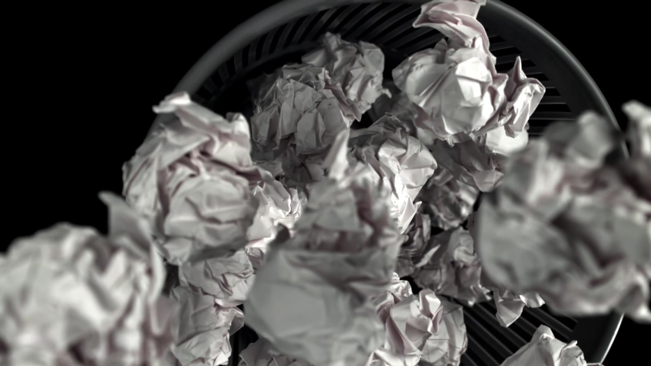 Molte palline di carta accartocciate che riempiono un cestino.