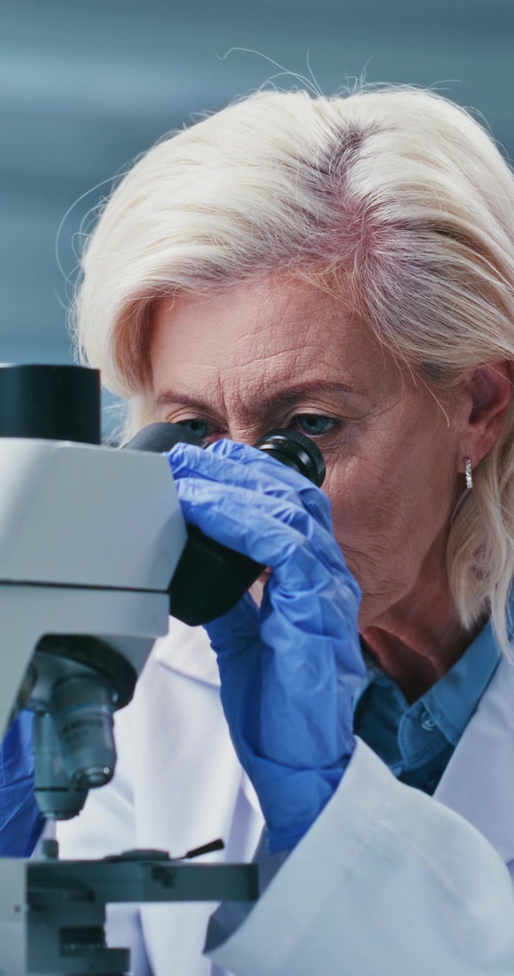 Scienziata anziana che esamina campioni al microscopio in laboratorio