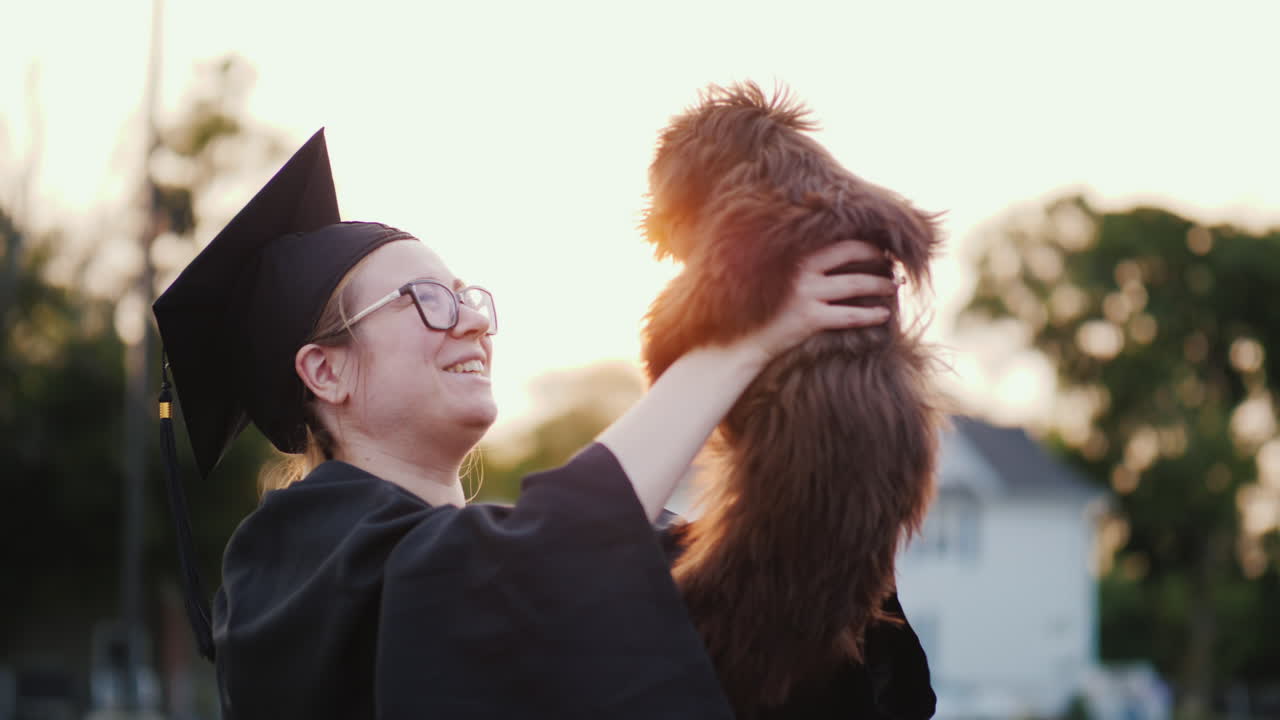 졸업 의상을 입은 여자가 대학 졸업 선물에 귀여운 강아지를 안고 있다