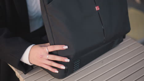 close-up of lady with rings and polished nails unzipping a sleek black bag on a wooden table and opening it to reveal a laptop inside, in a professional and modern setting