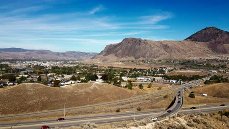 Push-in-Drone-Shot-of-Cars-and-Trucks-driving-on-Highway-1-and-the-Yellowhead-Highway-in-the-City-of-Kamloops,-Thompson-Okanagan-in-British-Columbia-on-a-sunny-day-in-a-desert-env
