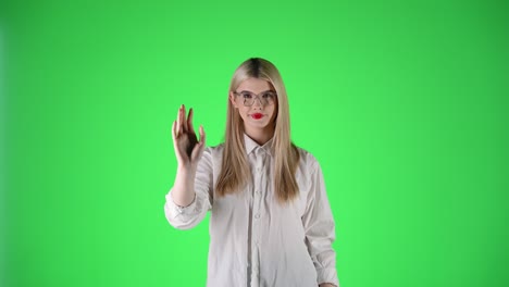 woman with red lipstick and white shirt waves in greeting, green background