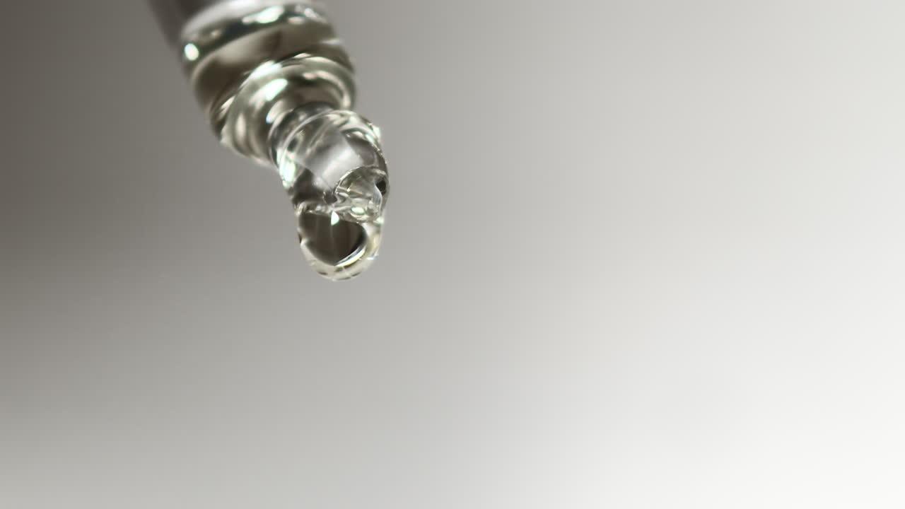 Goccia d'acqua che si forma lentamente sull'estremità di una pipetta da laboratorio in vetro, macro, isolato