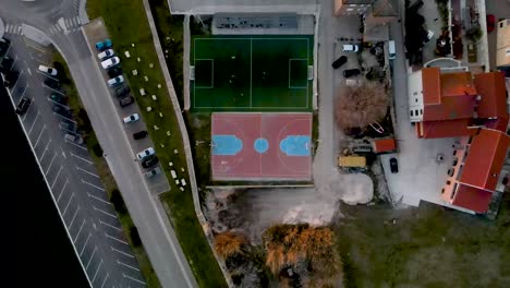 high drone flight from bird's eye view over a small soccer field next to an basketball field where a game is being played near a street with cars