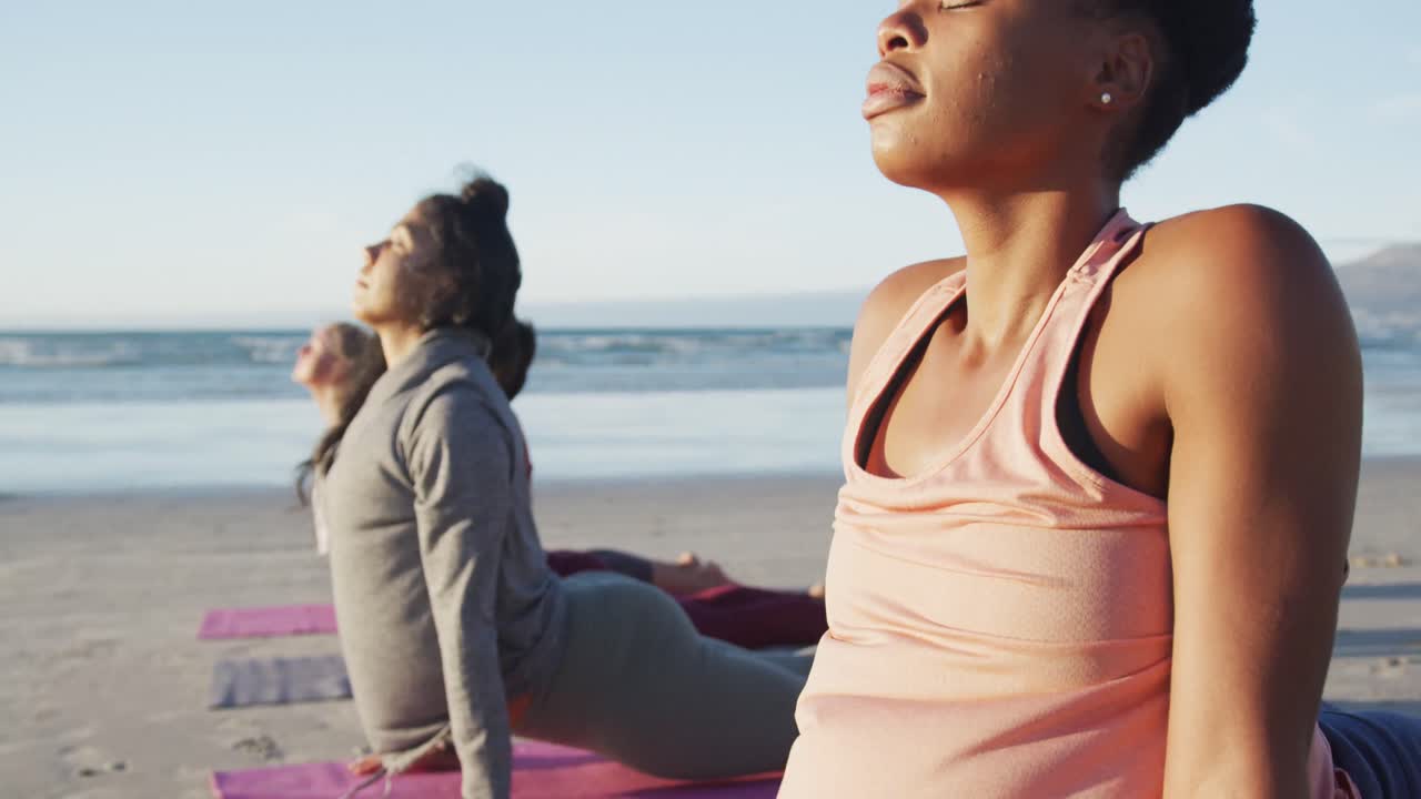 Group of diverse female friends practicing yoga, stretching at the beach