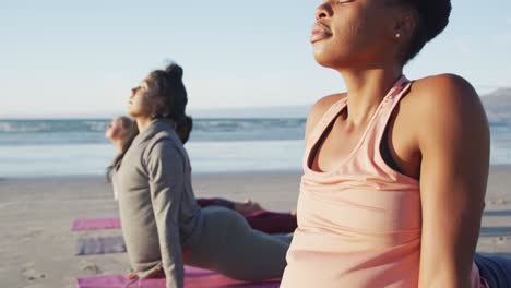 group of diverse female friends practicing yoga, stretching at the beach