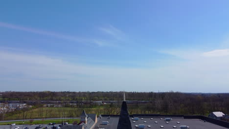 a drone rises from a retail clock tower in lancaster, pa, revealing the commercial building's rooftop before expanding into a sweeping view of surrounding fields, trees, and the open countryside.