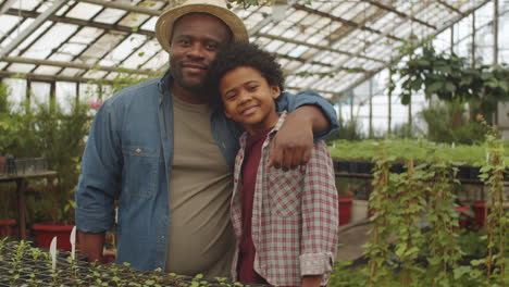 portrait of happy african american farmer with son in greenhouse