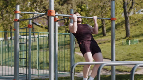 hombre libanés atlético en ropa deportiva haciendo ejercicios de pull ups en una barra horizontal, bombeando la espalda