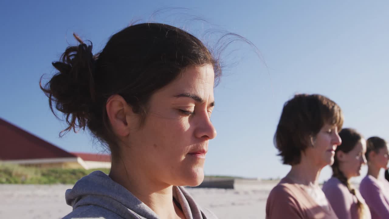 grupo multiétnico de mujeres haciendo posición de yoga en la playa y fondo de cielo azul