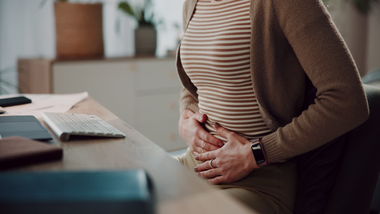 Woman Sitting at Desk Holding Her Stomach in Pain