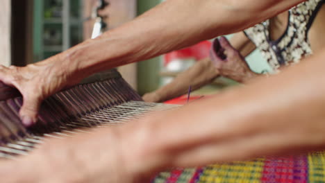 Close-up-view-of-old-female-hands-making-colorful-handmade-traditional-mattress-in-Quang-Nam-province,-Vietnam-in-a-handloom