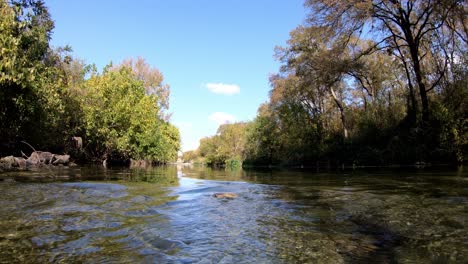 sentado al nivel del agua, girando hacia la izquierda pasando por una gran área abierta del arroyo mientras el agua revolotea y ondula desde la corriente.