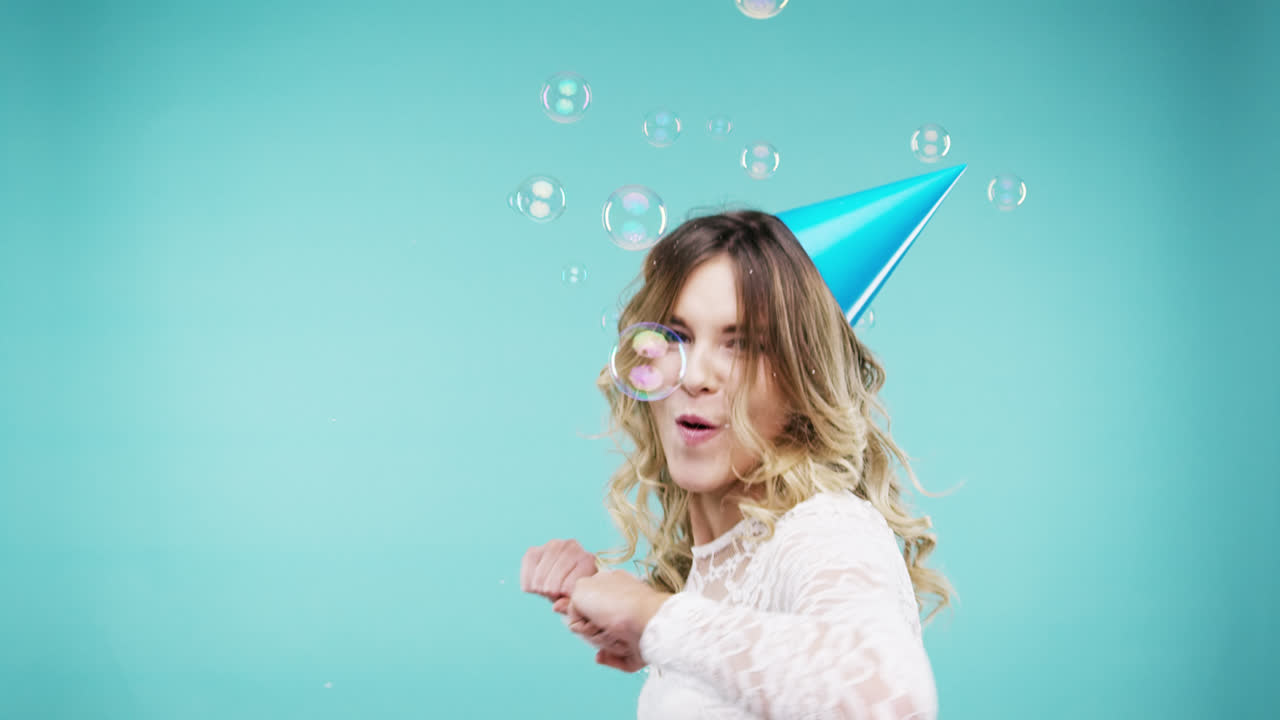 Frau mit lustigem Gesicht tanzt in Schaumbad-Dusche in Zeitlupe, Fotobox, blauer Hintergrund.