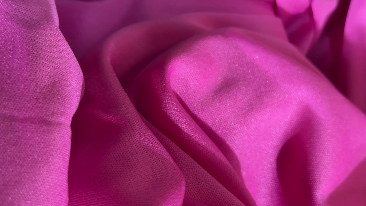 Primo piano di texture di tessuto rosa vibrante con pieghe morbide.