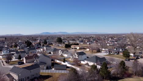 Drone-Volando-Hacia-Arriba-Enfocándose-En-Un-árbol-Sin-Hojas-Del-Invierno-Para-Revelar-Un-Hermoso-Barrio-Suburbano-Americano-Con-Montañas-En-El-Fondo-Distante-En-Un-Soleado-Día-De-Primavera