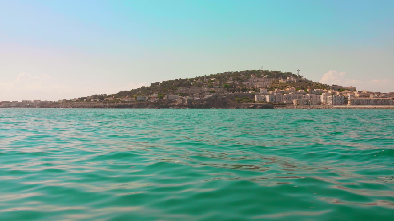 A smooth boat-level shot approaching the coastline of Sète, France, with the city’s hillside buildings under clear afternoon skies