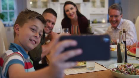 nieto caucásico feliz tomando una selfie con los padres y el abuelo en la mesa durante la comida familiar