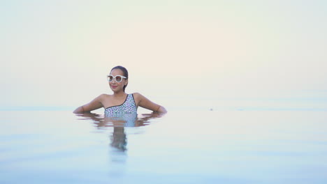 an attractive woman relaxing at a hotel while leaning on the edge of a rooftop resort infinity pool in thailand daytime