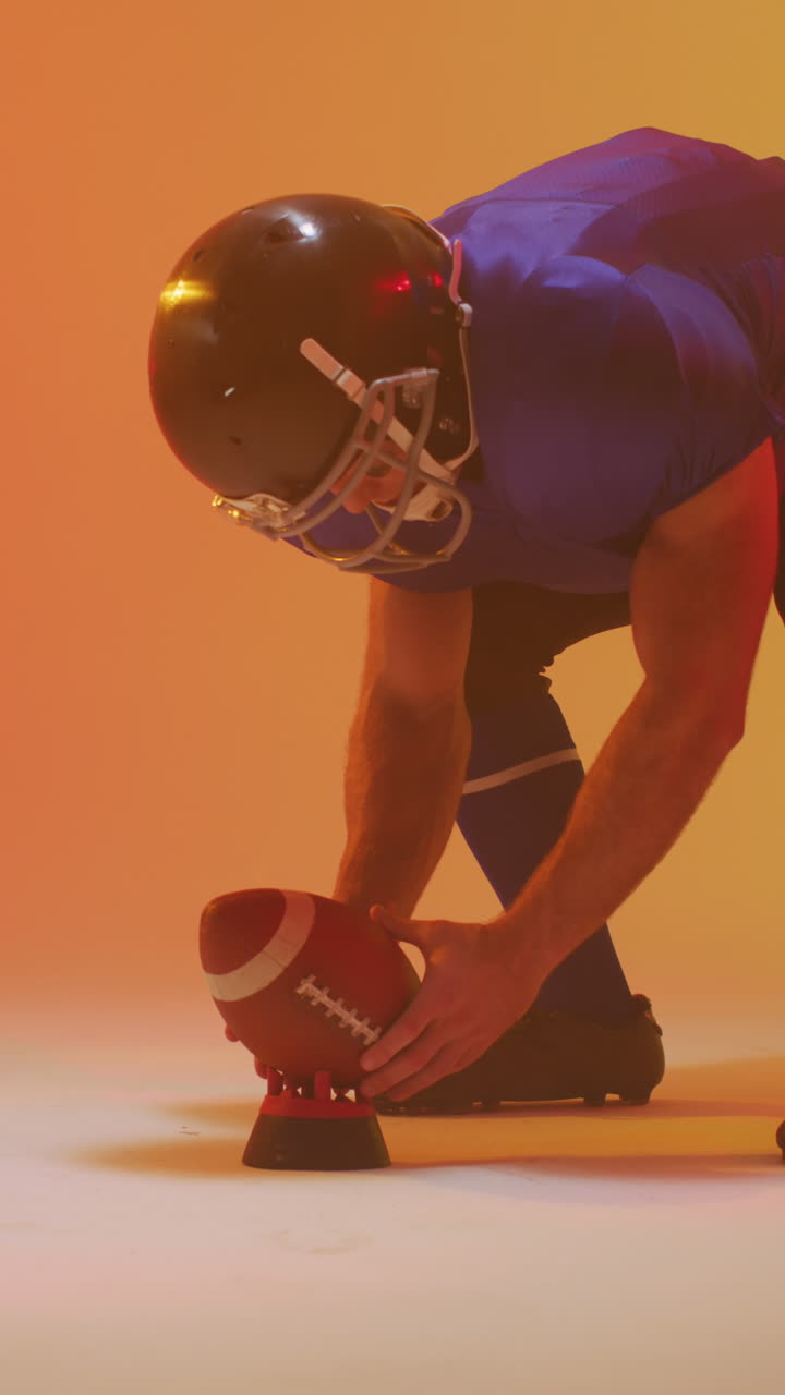 video vertical de un jugador de fútbol americano caucásico masculino sosteniendo la pelota, con iluminación naranja de neón