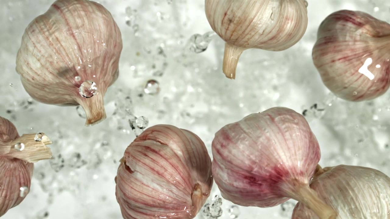 Bulbi d'aglio freschi che galleggiano e schizzano in acqua pulita.